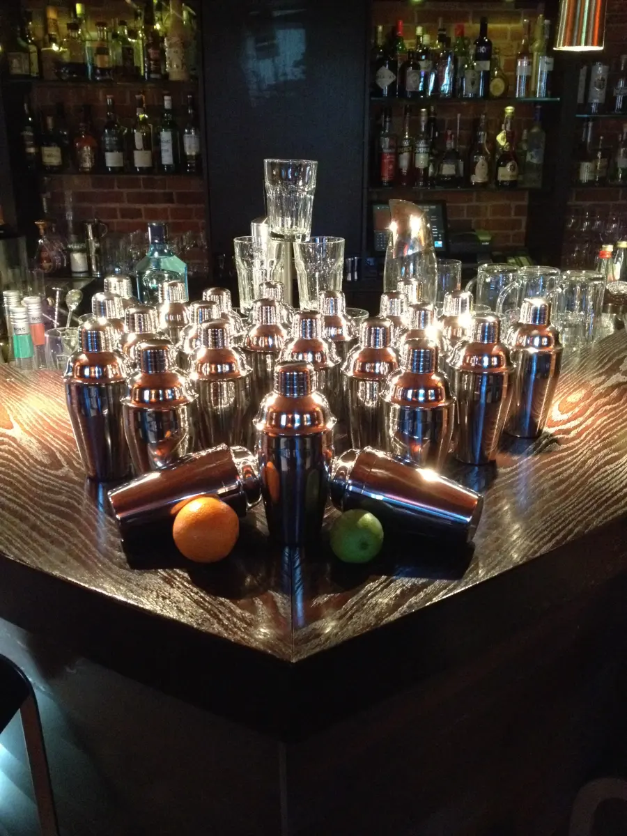 Viele Cocktailshaker auf dem Tresen, davor eine Orange und eine Limette